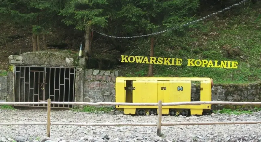 Wejście do sztolni Kowary z żółtym wagonikiem górniczym i napisem "KOWARSKIE KOPALNIE".