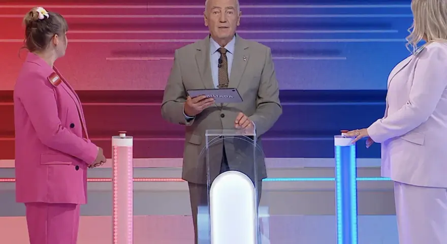 Prowadzący Familiady z tabliczką "Miliada" i dwie uczestniczki w różowych strojach. Zastanawiają się, co zmieniamy podczas jazdy samochodem.