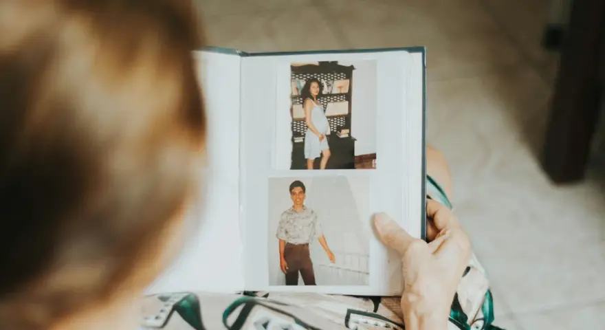 Osoba przegląda fotoksiążkę ze zdjęciami z ciąży i młodzieńczymi portretami. To inspiracja, jak zrobić fotoksiążkę pełną wspomnień.