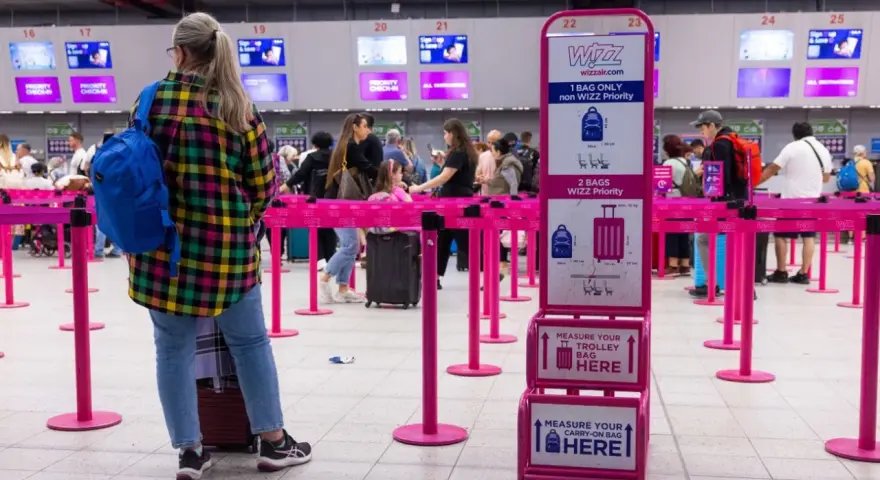 Kolejka do odprawy Wizzair. Tablica informuje, co trzeba wyjąć z bagażu podręcznego: płyny, elektronikę i przedmioty ostre.