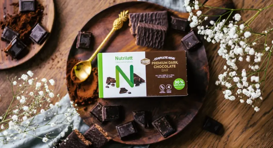 Chokladbitar och en förpackning med Nutrilett Premium Dark Chocolate Bar, en del av deras kalorisnål mat-sortiment.