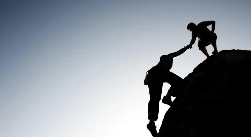 Silhouette d'un grimpeur aidant un autre à atteindre le sommet. Une belle présentation photographe de l'entraide et de la persévérance.