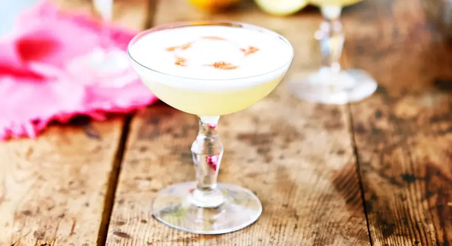 En krämig pisco sour med ett vitt skum och en touch av kanel på en rustik träyta.