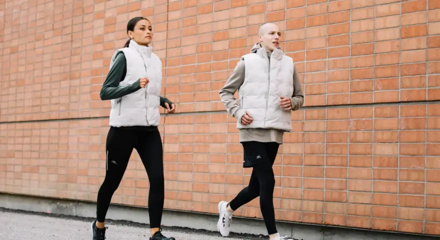 Coppia corre lungo un muro di mattoni. Ottimi consigli per correre in coppia, con abbigliamento tecnico.