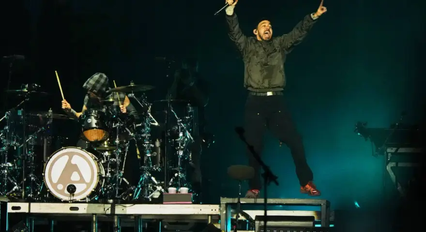 Linkin Park-Bandmitglieder auf der Bühne, ein Sänger springt, ein Schlagzeuger spielt.
