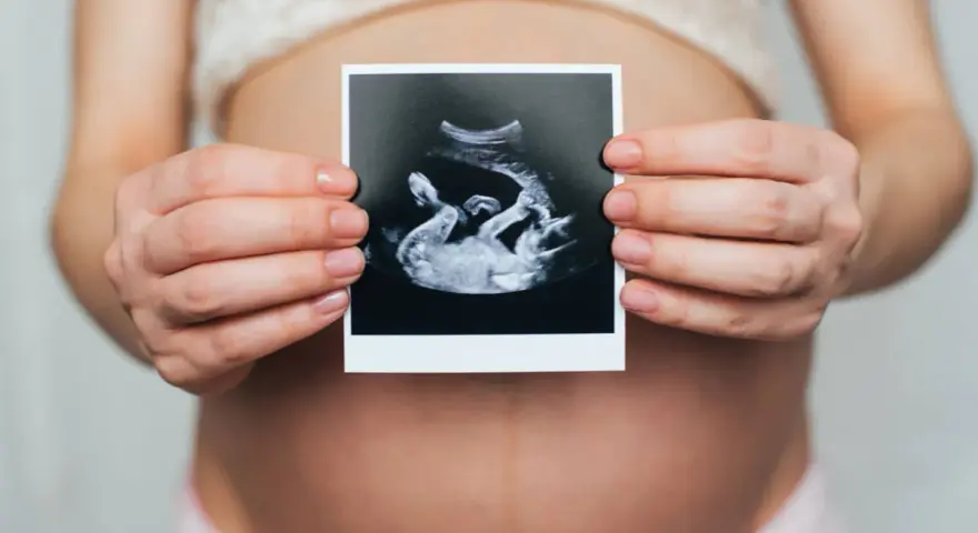 Ciężarna kobieta trzyma zdjęcie USG, na którym widać dziecko. Widać też łożysko na przedniej ścianie.