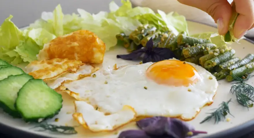 Un œuf au plat parfait, servi avec des haricots verts, des tranches de concombre, de la laitue et une touche de citron vert.