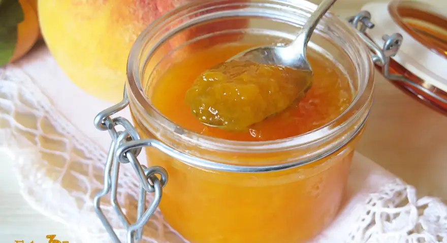 Cuchara con mermelada de melocotón casera, junto a melocotones frescos y un tarro de cristal.