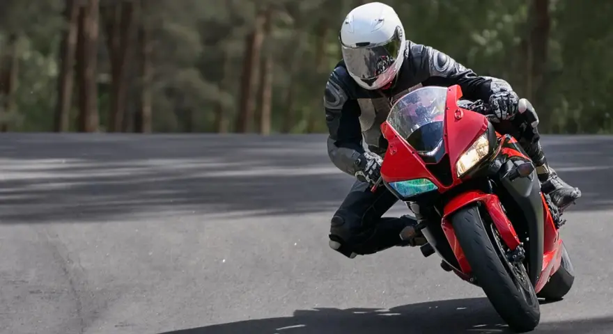 Motocyklista w białym kasku i czarnym kombinezonie pochyla się na czerwonym motocyklu podczas jazdy po drodze.