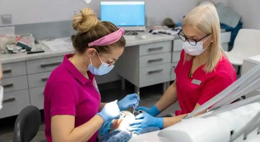 Dwie dentystki w różowych uniformach pracują przy pacjencie. Zastanawiasz się, po jakim czasie działa lekarstwo w zębie?