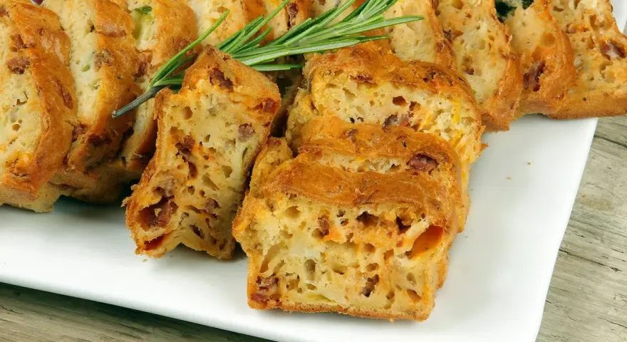 Tranches d'un cake salé au chorizo et poivron, garni de romarin, sur une assiette blanche.