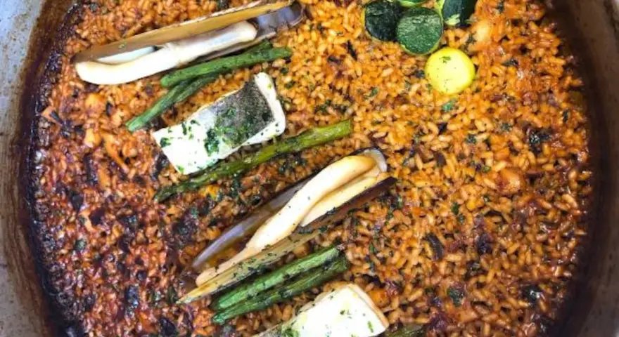 Deliciosa paella valenciana con arroz dorado, espárragos, pescado y navajas.