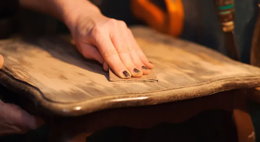Main d'une personne ponçant un meuble en bois pour enlever la cire naturellement.