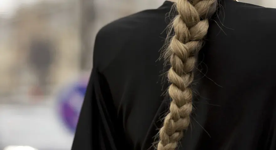 Gruby, blond warkocz opada na czarne ramię. To jedna z tych fryzur z warkoczem, które przyciągają wzrok.