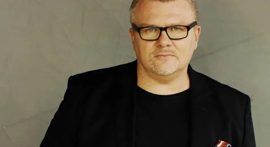 Rafał Michalak w czarnym garniturze i okularach, z charakterystyczną bródką. W kieszeni marynarki ozdobna poszetka.