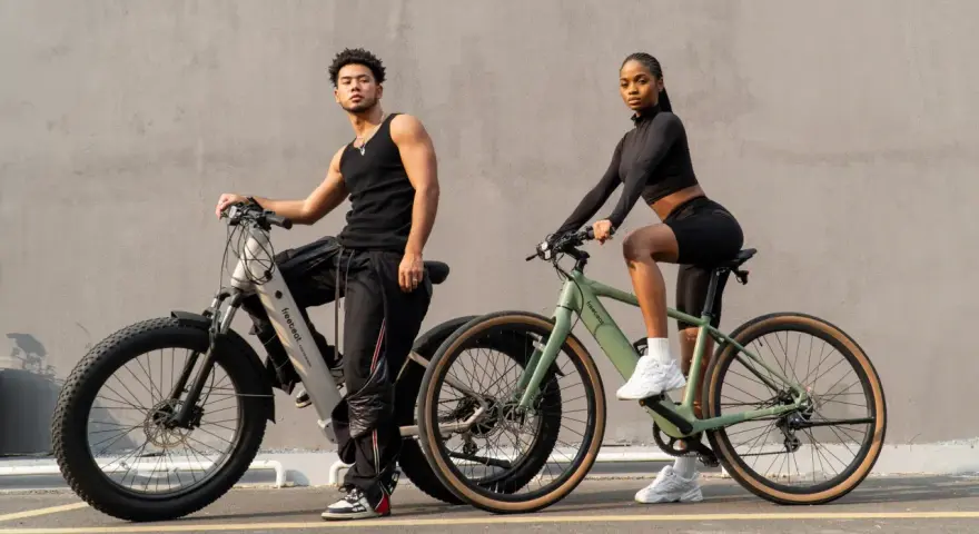 A man and woman pose with their electric hybrid bikes, showcasing a blend of urban style and off-road capability.