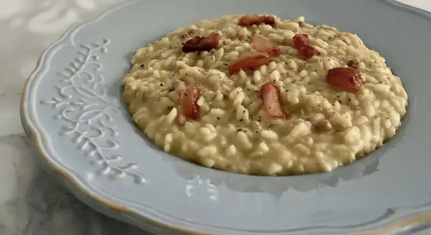Un cremoso risotto con ceci e pancetta croccante, servito su un piatto azzurro decorato.