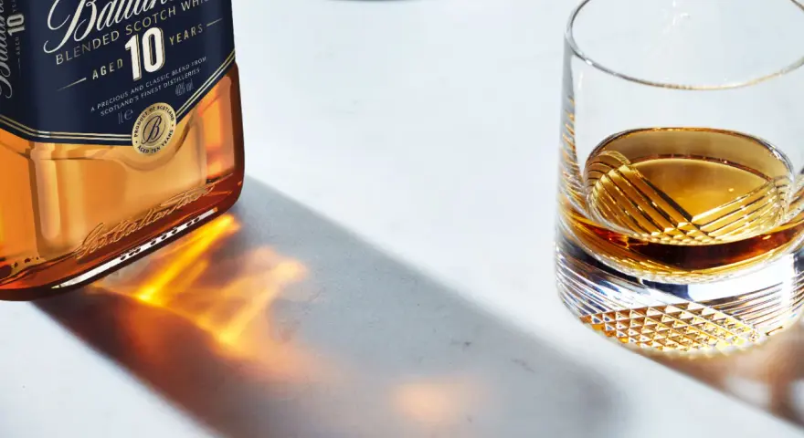 Butelka Ballantine's 10 Years Old i szklanka z bursztynowym płynem, przypominającym smak bourbona.