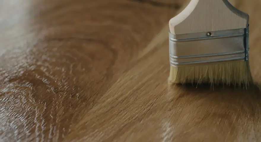 Brocha aplicando un acabado brillante sobre madera, mostrando diferentes tipos de barniz para madera.