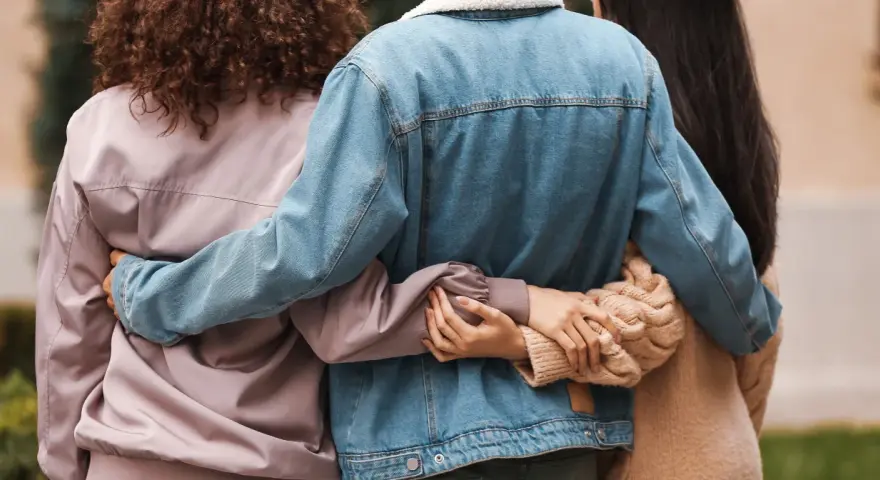 Trzy osoby obejmują się. Ich bliskość symbolizuje wsparcie i przyjaźń, nawet jeśli tworzą związek bez mieszkania razem.