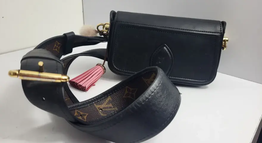 Elegancka, czarna louis vuitton torebka z ozdobnym, różowym pomponem i paskiem z monogramem.