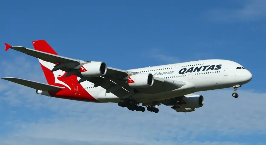 Gros avion Qantas, avec son logo rouge et blanc emblématique, en plein vol sous un ciel bleu.