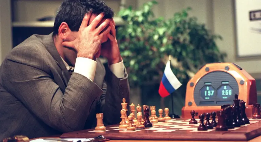 Garry Kasparov, le visage dans les mains, face à Deep Blue. L'horloge d'échecs affiche 1:57 et 1:56.