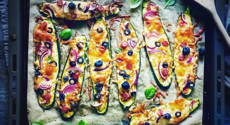 Zucchini-Hälften mit Käse, Oliven, Zwiebeln und Salami, die wie Pizza belegt sind. Sie schmeckt zucchini auf pizza!