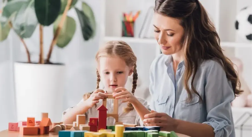 Kobieta i dziewczynka budują wieżę z kolorowych klocków.