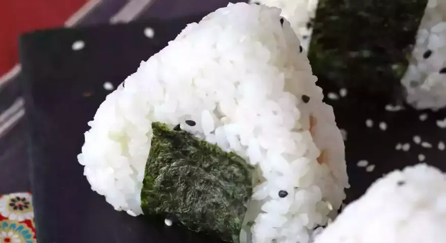 Trójkątne onigiri z tuńczykiem, ryżem i wodorostami nori, posypane sezamem.