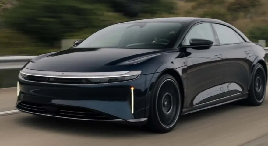 Ciemnoniebieski Lucid Air Sapphire pędzi po drodze, jego aerodynamiczna sylwetka i futurystyczne światła przyciągają wzrok.