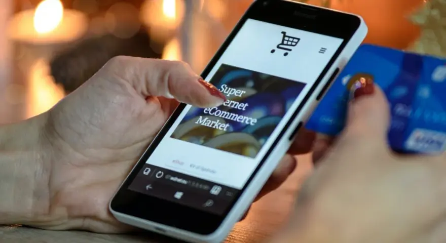 Kobieta z kartą kredytową w dłoni przegląda na smartfonie stronę e-commerce, ucząc się, jak sprzedawać bieliznę w internecie.