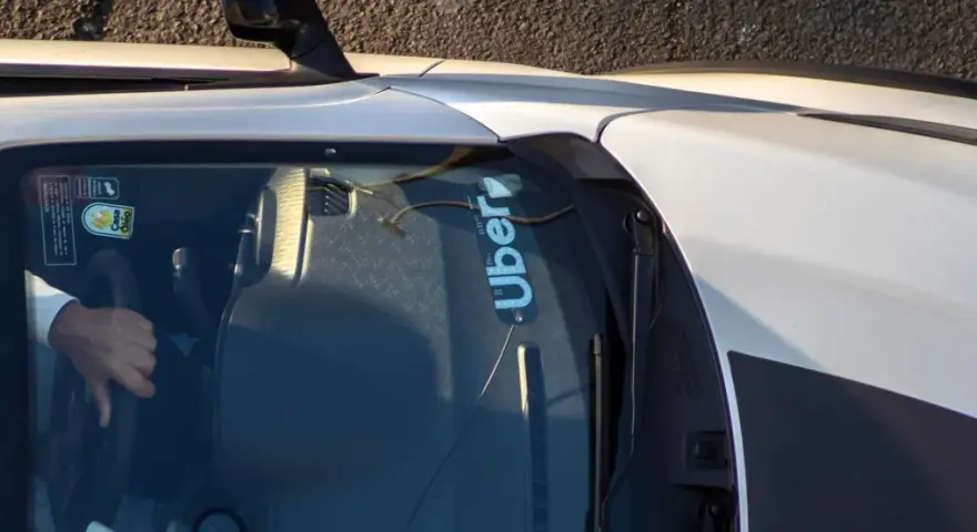 Fahrer hält das Lenkrad eines Autos mit Uber-Aufkleber auf der Windschutzscheibe.
