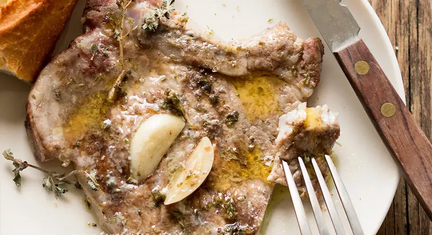 Succulenta braciola di maiale cotta con aglio e erbe aromatiche, servita con pane croccante.