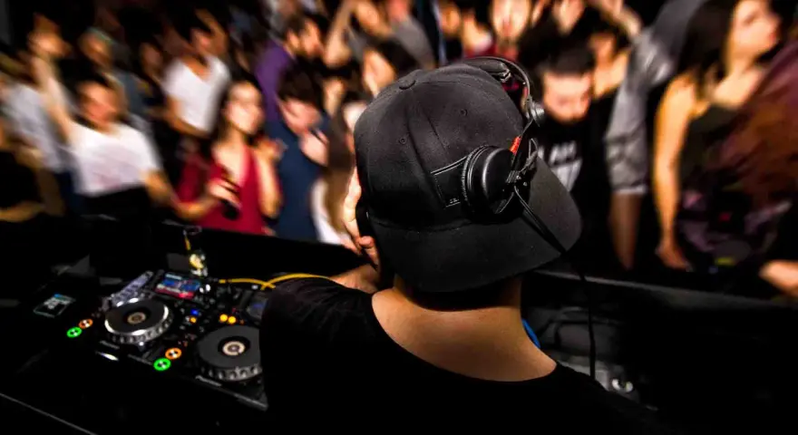 DJ aux platines, casque sur les oreilles, gérant le niveau sonore pour une foule en délire.