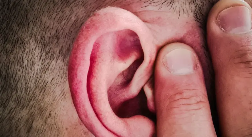 Un doigt pince l'oreille d'un homme, comme pour mieux capter un son aigu.