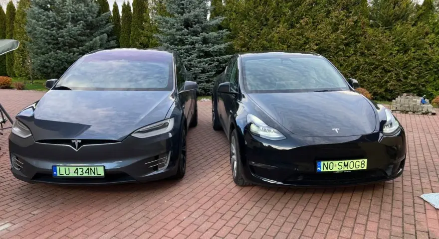 Dwa samochody Tesla, jeden ciemnoszary Model X, drugi czarny Model Y, stoją na podjeździe.