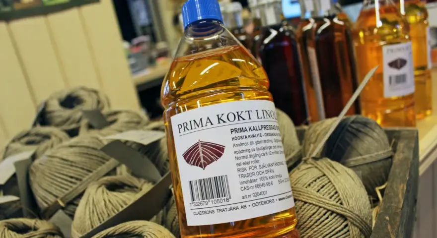 En flaska Prima kokt linolja, perfekt för fernissa oljemålning och ytbehandling av trä. Bredvid ligger härvor av garn.
