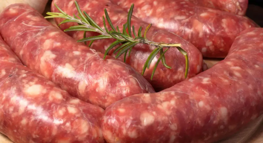 Salsiccia co to? Surowe kiełbaski wieprzowe, przyprawione ziołami, leżą na desce.