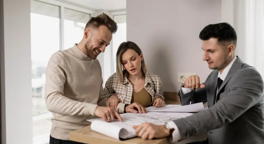 Un couple examine des plans avec un agent immobilier, illustrant l'obligation de l'agent immobilier envers l'acheteur.