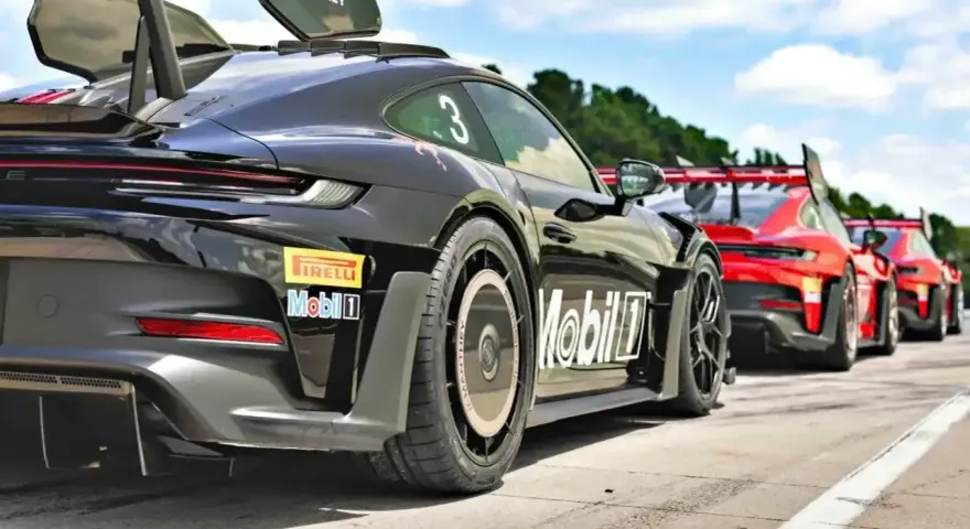 Czarny Porsche GT3 RS z numerem 3 i logo Manthey na skrzydle, gotowy do wyścigu obok czerwonych samochodów.