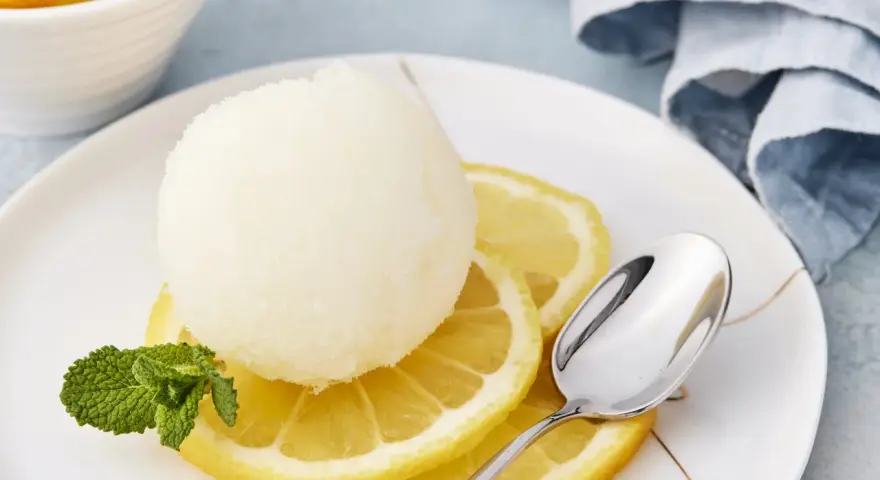 Erfrischendes Zitronensorbetto-Rezept: Eine Kugel Sorbet auf Zitronenscheiben mit Minze und Löffel.