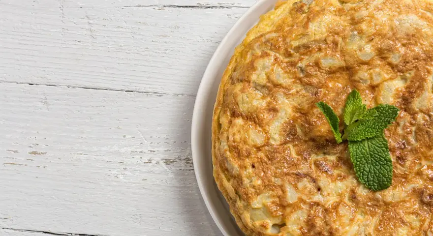 Frittata di cipolle dorata e soffice, guarnita con foglie di menta fresca, su un piatto bianco appoggiato su un tavolo di legno sbiancato.