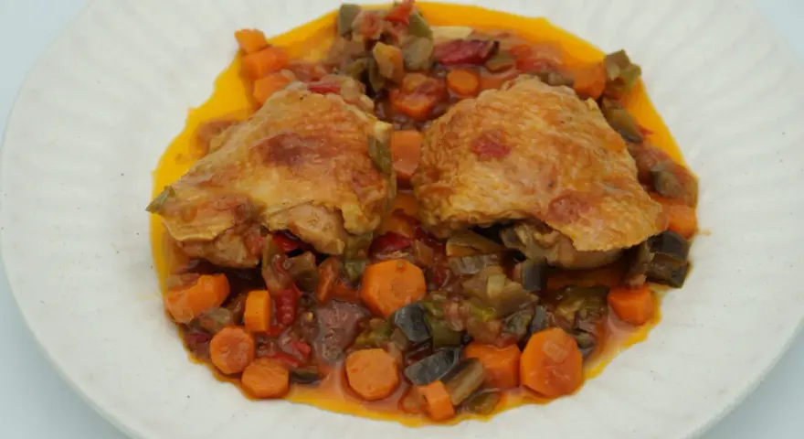 Dos piezas de pollo dorado sobre un guiso de verduras coloridas, zanahorias y berenjenas. Un delicioso pollo a la jardinera.