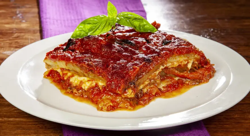 Una fetta di parmigiana di melanzane napoletana, ricca e saporita, guarnita con basilico fresco.