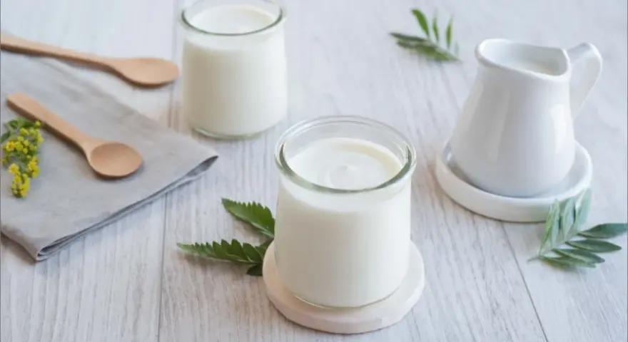 Deux pots de yaourt, une petite cruche et des cuillères en bois sur une table. La couleur blanche du lait, pourquoi est-il si pur ?