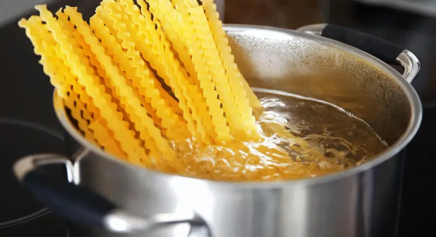 Lange, gewellte vermicelli noodles kochen in sprudelndem Wasser in einem Edelstahltopf.