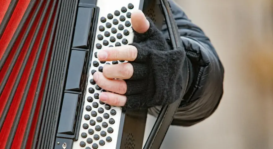 Dłoń w rękawiczce gra na akordeonie, wydobywając dźwięki tego wyjątkowego instrumentu.
