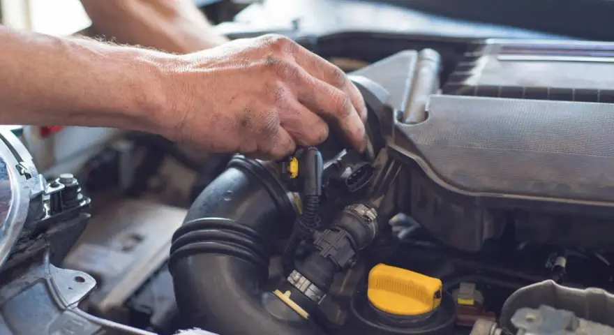 Ręce mechanika pracują przy silniku samochodu. Widoczny jest czarny przewód dolotowy i żółta zakrętka. p0101.