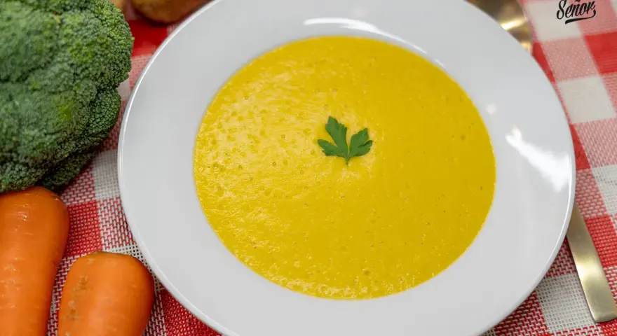 Un cremoso puré de verduras, con brócoli y zanahorias frescos al lado, listo para disfrutar.
